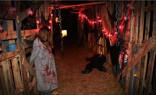 A dimly lit, eerie corridor with blood-stained walls, chains, and red lights, featuring a figure and a lifeless body.