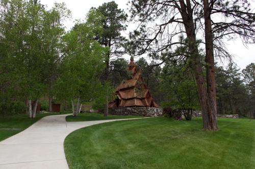 A winding path leads to a unique wooden building surrounded by lush green trees and grass.
