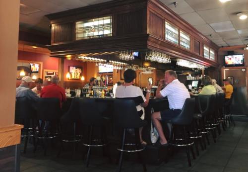 A busy bar with patrons seated at high stools, enjoying drinks and conversation in a warm, inviting atmosphere.