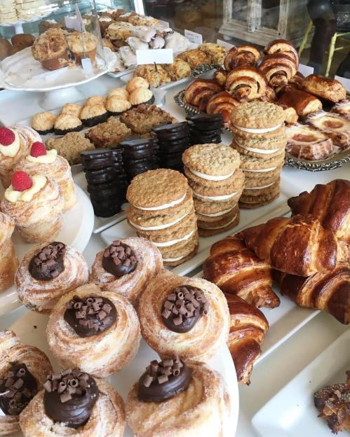 A variety of baked goods including pastries, cookies, and cinnamon rolls displayed on white plates.