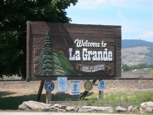 Welcome sign for La Grande, Oregon, featuring trees and mountains, with logos of local organizations below.