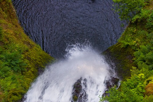 A waterfall cascading into a dark pool, surrounded by lush green foliage and rocky terrain.