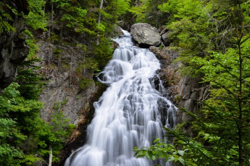 A cascading waterfall flows down rocky cliffs, surrounded by lush green trees and foliage.
