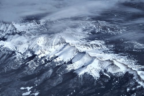 Aerial view of snow-covered mountains with clouds partially obscuring the peaks and valleys below.