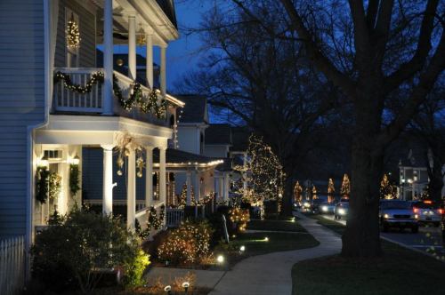 A festive street scene at night, with houses adorned in holiday lights and decorations, creating a warm, cheerful atmosphere.