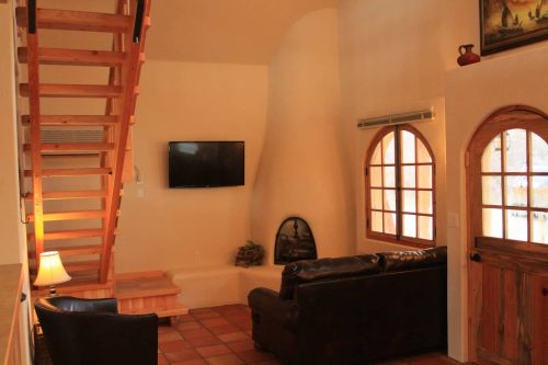 Cozy living area with a staircase, TV, fireplace, and wooden accents, featuring a leather couch and warm lighting.