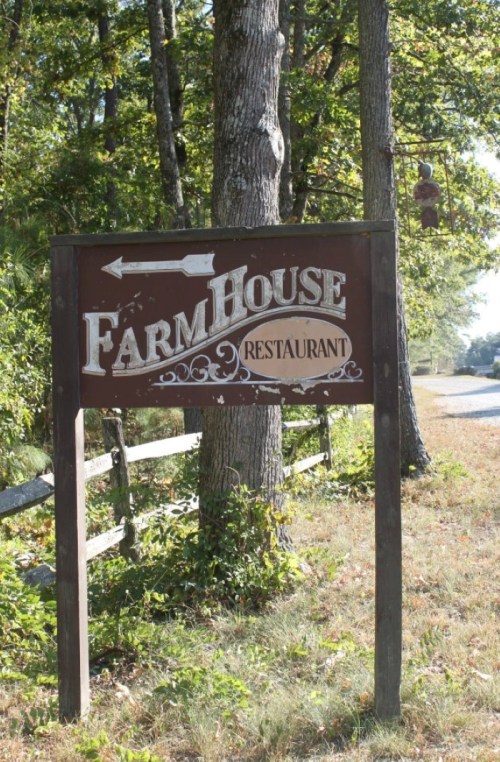 Sign for "Farm House Restaurant" with an arrow pointing left, surrounded by trees and grass.
