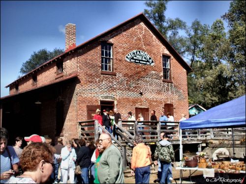 A historic brick building with a sign, surrounded by a crowd of people at an outdoor event.