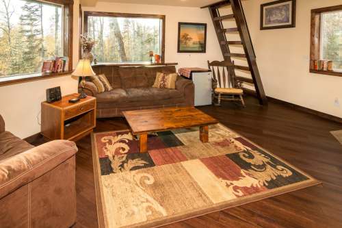 Cozy living room with a brown couch, wooden coffee table, and large windows overlooking a forested area.