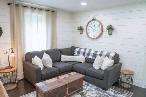Cozy living room with a gray sectional sofa, decorative pillows, a wooden coffee table, and a large wall clock.