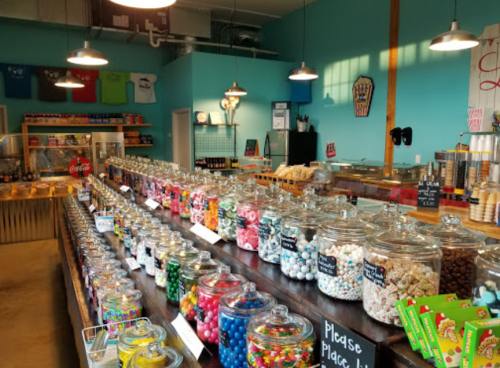A colorful candy shop interior with jars of sweets, snacks, and a counter for ice cream and drinks.