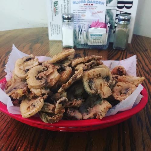 A red basket filled with crispy fried mushrooms, served with a side of condiments in a casual dining setting.