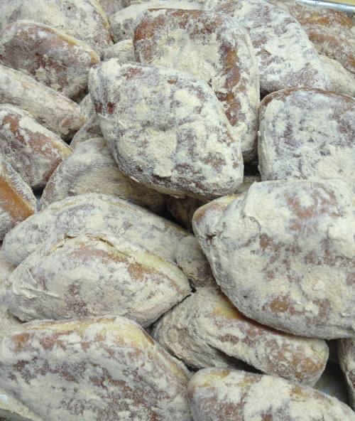 A close-up of a pile of flour-dusted pastries, showcasing their textured surfaces and irregular shapes.