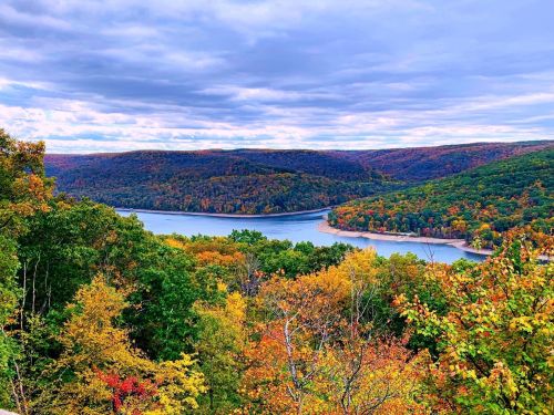 A scenic view of a river winding through colorful autumn foliage and rolling hills under a cloudy sky.