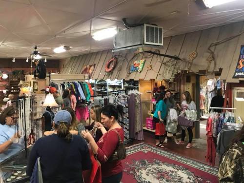 A busy retail store interior with shoppers browsing clothing and accessories, featuring racks and displays.