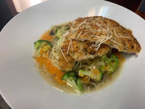 A plate of breaded fish fillets served over pasta and mixed vegetables, topped with grated cheese.