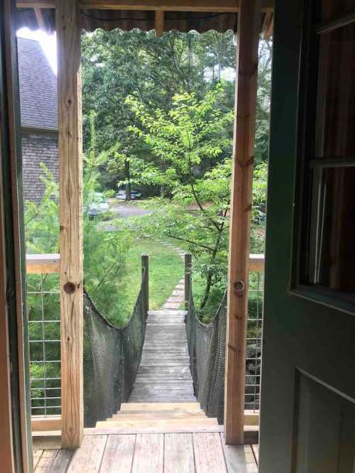 View from an open door showing a wooden walkway leading to a green yard surrounded by trees.