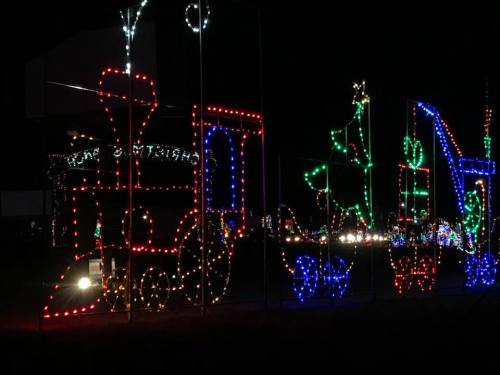 Colorful holiday lights form a train, Christmas tree, and presents against a dark night sky.