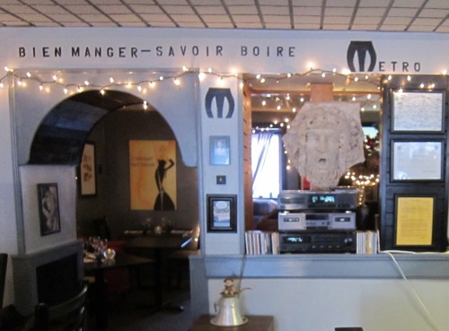 Interior of a cozy restaurant with string lights, a decorative arch, and a wall featuring art and a lion's head sculpture.
