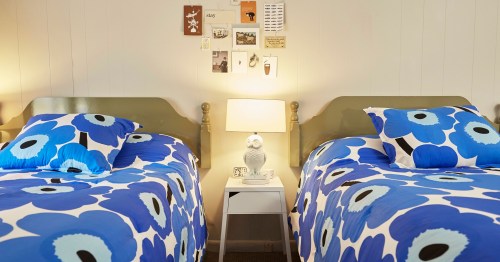 Two twin beds with blue floral bedding, a nightstand with a lamp, and wall decor in a cozy room.