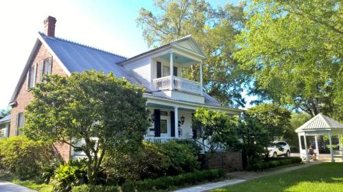 A charming two-story house with a porch, surrounded by lush greenery and a gazebo in the yard.