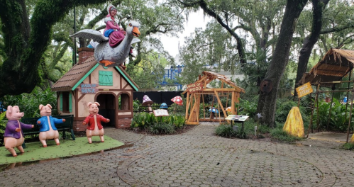 Colorful fairy tale scene featuring three pigs, a house, and a character riding a large bird in a lush garden setting.