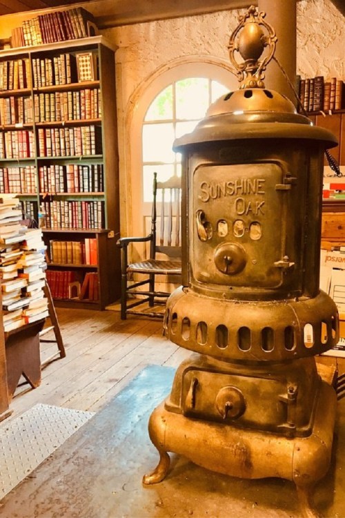 A vintage cast-iron stove in a cozy library filled with books and a wooden chair by a window.