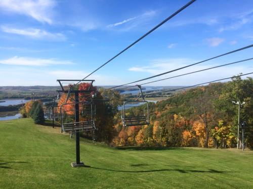 A ski lift on a grassy hill with colorful autumn trees and a scenic view of a lake and rolling hills in the background.