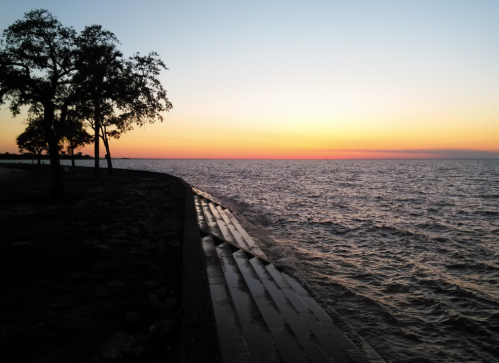 Sunset over a calm lake, with silhouettes of trees and a shoreline reflecting the warm colors of the sky.