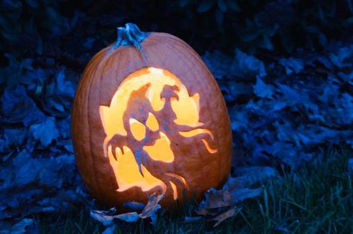 A carved pumpkin glowing with a spooky design, surrounded by fallen leaves in a dark setting.