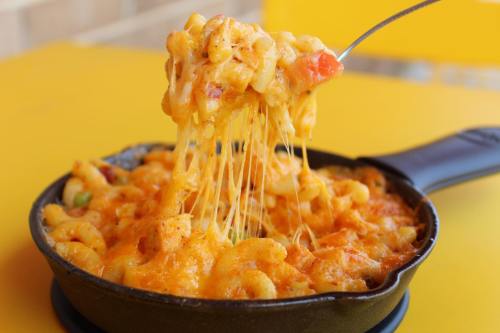 A cheesy macaroni and cheese dish in a skillet, with gooey cheese stretching from a spoon.