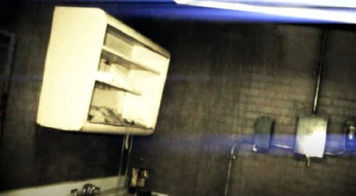 A dimly lit room with a wall-mounted cabinet and exposed pipes, creating an eerie atmosphere.