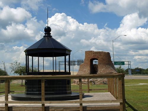 A gazebo next to the ruins of a brick structure, set against a cloudy sky and highway signs in the background.