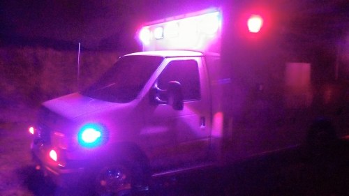 An ambulance with flashing blue and red lights parked at night, surrounded by darkness.
