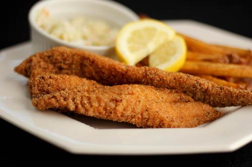 A plate featuring two crispy fried fish fillets, lemon slices, coleslaw, and golden French fries.