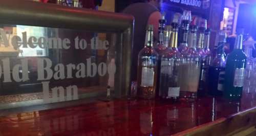 A bar counter with various bottles of liquor and a sign reading "Welcome to the Old Baraboo Inn."