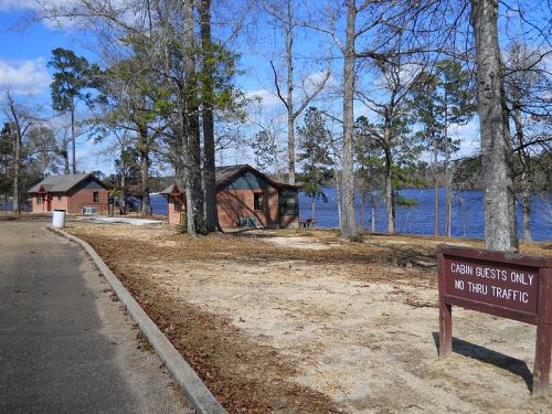 A scenic view of cabins by a lake, surrounded by trees, with a sign indicating "Cabin Guests Only, No Thru Traffic."