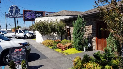 Exterior view of Da Wabbit Drive-In with greenery, a stone facade, and parked cars under a clear blue sky.