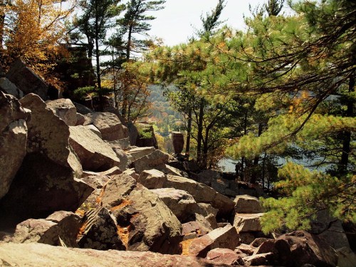 A rocky landscape surrounded by trees, with autumn foliage and a view of a lake in the background.