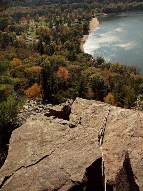 A scenic view from a rocky ledge overlooking a lake and forested area with autumn foliage.