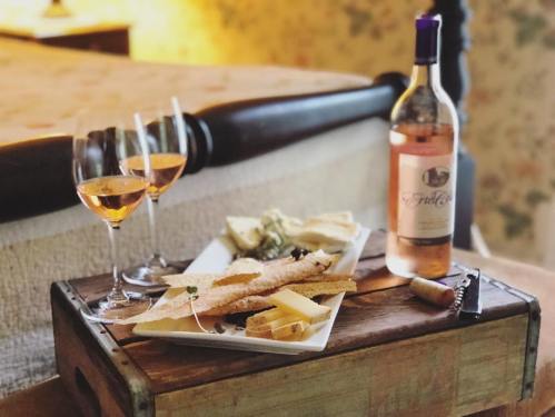 A cozy setting with three glasses of rosé wine, a platter of cheese, and a bottle of wine on a wooden tray.