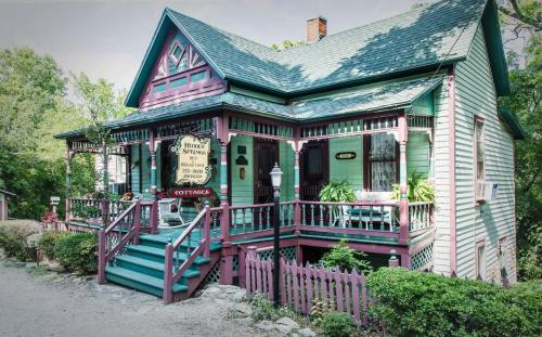 A charming, colorful cottage with a green and purple exterior, featuring a sign for "House of Springs" and lush landscaping.