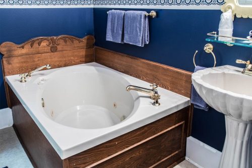 A vintage-style bathroom featuring a wooden bathtub, gold faucets, and a white sink against a dark blue wall.