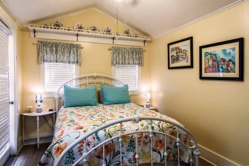 Cozy bedroom with a floral bedspread, two lamps, and colorful artwork on the walls. Bright and inviting atmosphere.