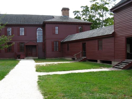 A red wooden building with multiple sections, surrounded by a grassy area and a gravel path.