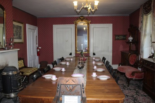 A vintage dining room with a long wooden table set for tea, ornate decor, and a large mirror on the wall.