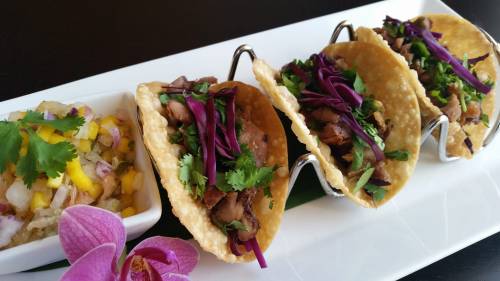 Three tacos filled with meat, topped with purple cabbage and cilantro, served with a side of mango salsa.