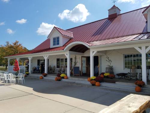 A charming white building with a red roof, surrounded by pumpkins and flowers, on a sunny day.