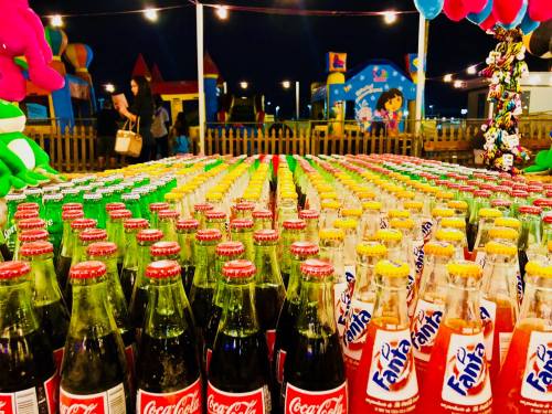 A colorful display of Coca-Cola and Fanta bottles arranged in rows at a festive outdoor event.