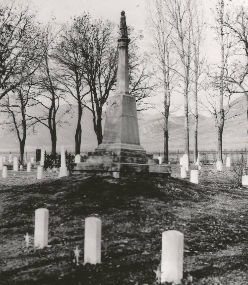 A historic cemetery with a tall monument surrounded by gravestones and bare trees in the background.